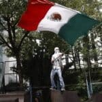 Persona sosteniendo una bandera de México durante una protesta.